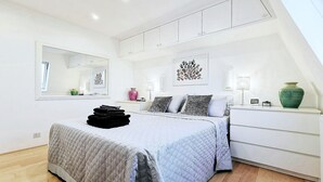 Ein modernes Schlafzimmer mit Bett, Nachttischen, einem Spiegel und Kunstwerken an den Wänden.