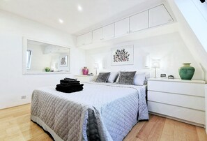 A modern bedroom with a bed, bedside tables, a mirror, and artwork on the walls. - Luxe modern Penthouse with A/C and two large beds.  Great location (London)