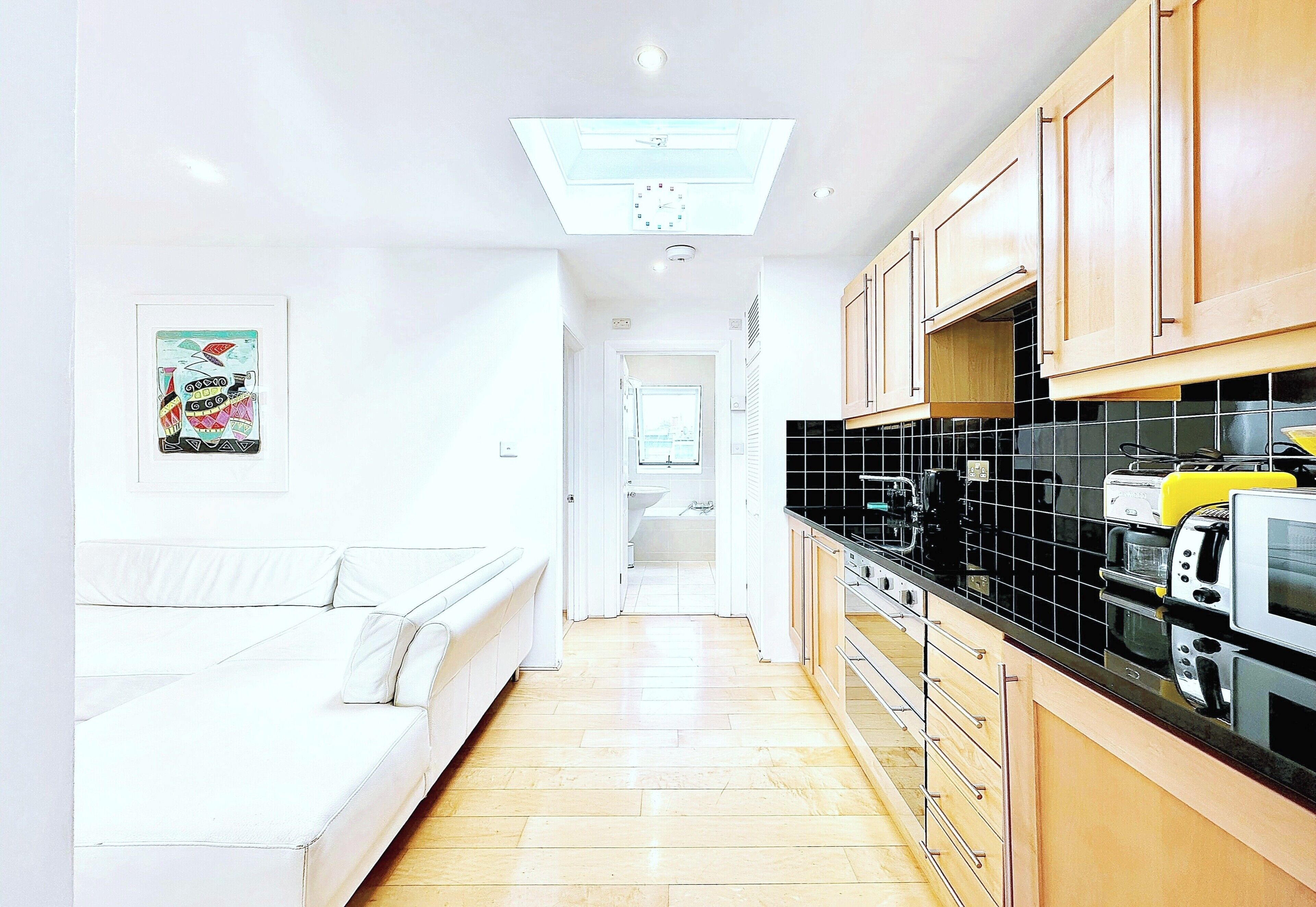 Une cuisine étroite avec un canapé blanc, des meubles de rangement en bois et un mur recouvert de carreaux.