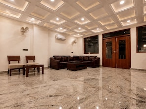 A spacious living area with a marble floor, a brown leather sofa, two wooden chairs, a coffee table, and a large window. - Hotel Woodmark - Sector 70 (Noida)