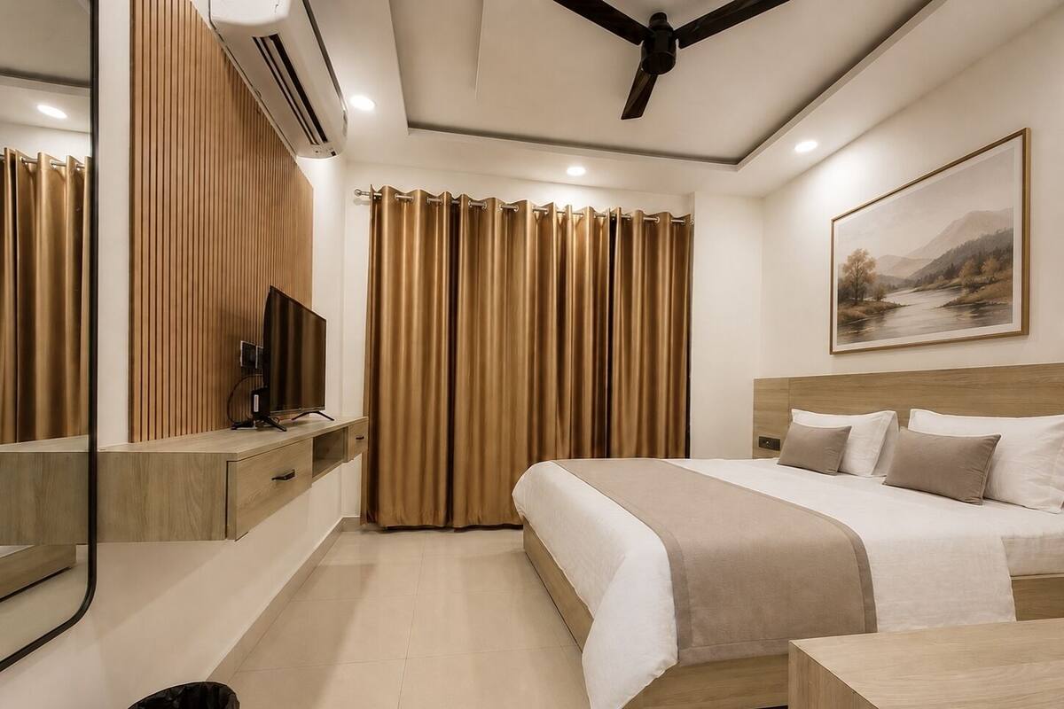 Habitación de hotel con cama, televisor, ventilador de techo, un cuadro y ventana con cortinas.