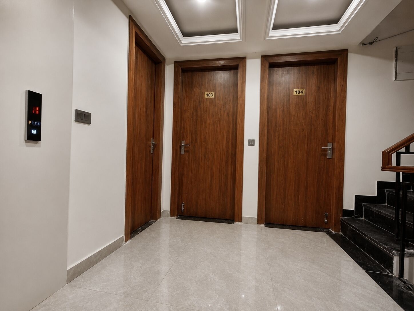 A hallway with three wooden doors, each marked with a number, and a digital elevator control panel.