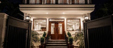 A two-story building with a balcony, a staircase leading to the entrance, and potted plants.