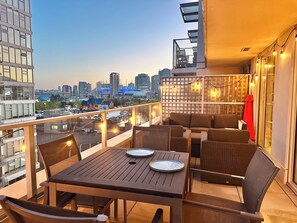 A balcony with a table and chairs, a city view, and string lights. - 2 bed, 2 bath, XL patio, short walk from stadium (Vancouver)