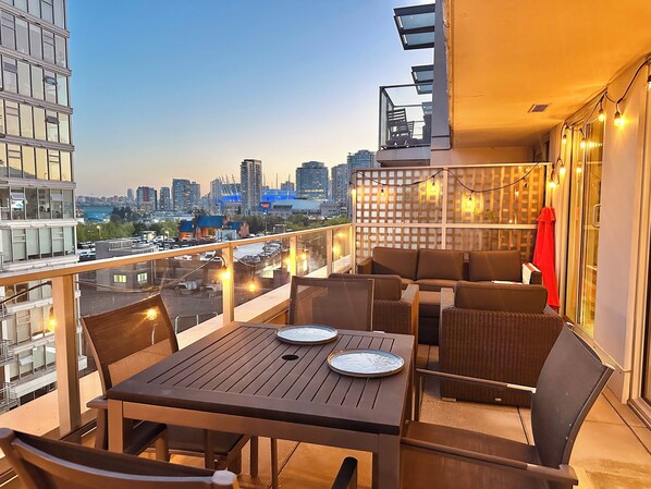 Ein Balkon mit Tisch und Stühlen, Blick auf die Stadt und Lichterketten.