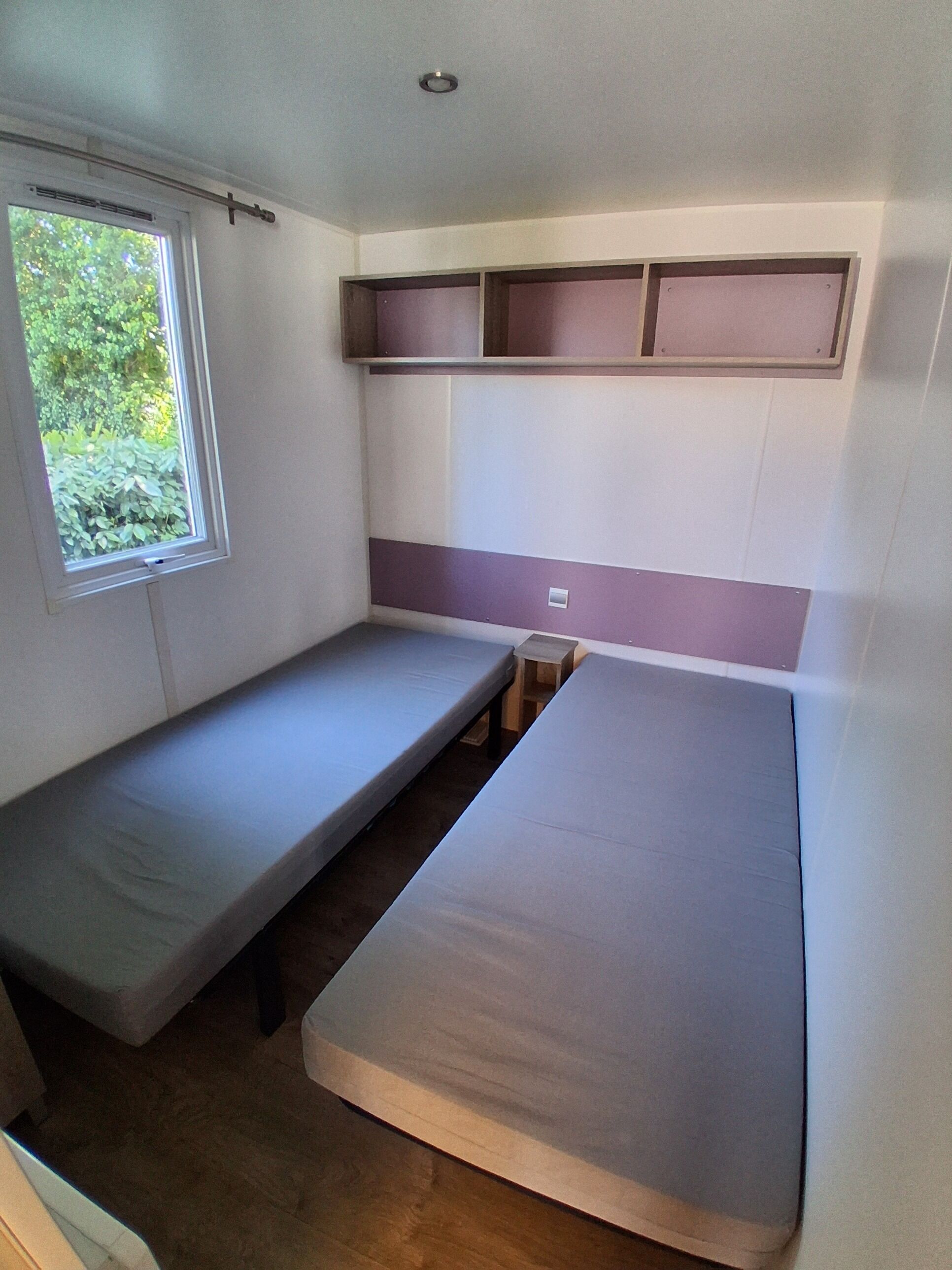 Een kleine kamer met twee eenpersoonsbedden, een raam en een ingebouwde plank.