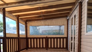 Eine überdachte Holzterrasse mit Blick auf ein Haus, Holzgeländern und einem klaren Himmel.