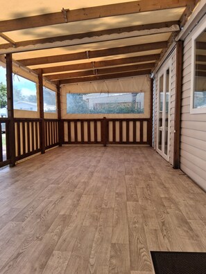 Eine überdachte Holzterrasse mit Blick auf ein Haus, Holzgeländern und einem klaren Himmel.
