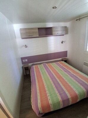 Ein kleines Schlafzimmer mit einem Bett, einem Nachttisch, einem Regal über dem Bett und einem Fenster.