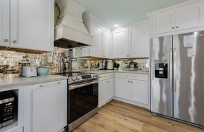 Une cuisine moderne avec des meubles blancs, des appareils électroménagers en acier inoxydable et un plancher en bois.