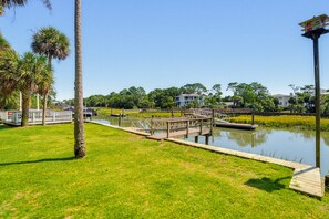 A waterfront park with a wooden dock, palm trees, and a building in the background. - 378 Wahoo Drive - Canal Front Home (Fripp Island)