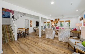 A spacious living area with a wooden floor, a dining table, and a staircase leading to an upper level. - 378 Wahoo Drive - Canal Front Home (Fripp Island)