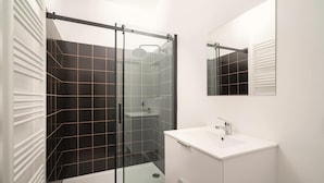 Un baño moderno con cabina de ducha de vidrio, un lavabo blanco y un espejo.