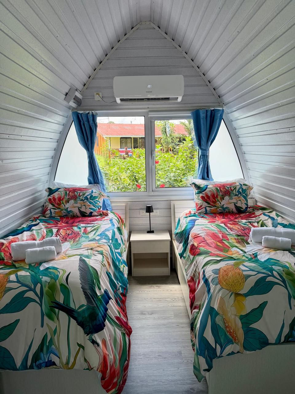 A bedroom with two beds, a window with curtains, and an air conditioning unit.