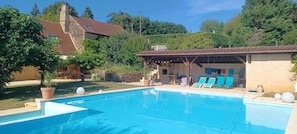 A swimming pool with lounge chairs, a covered patio, and a stone house with a tiled roof. - Stone cottage Dordogne, Périgord noir, between Sarlat and Bergerac (Alles-sur-Dordogne)