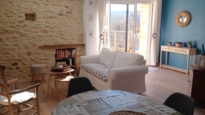 Una stanza accogliente con un muro in pietra, un divano bianco, un tavolo in legno e una libreria.