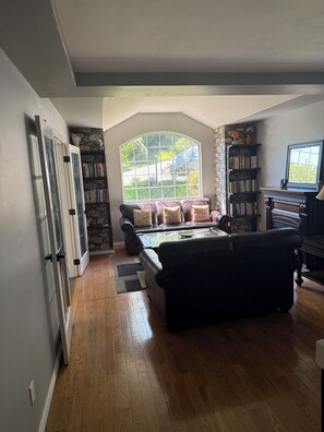 A living room with a fireplace, a stone wall, a bookshelf, and a large window.
