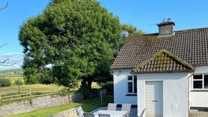 Ein Haus mit einem Ziegeldach, einer Satellitenschüssel und einer Terrasse mit Gartenmöbeln.