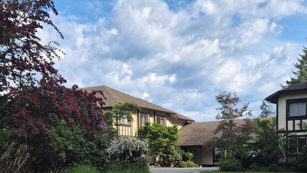 A paved pathway leading to a building with a sloped roof, surrounded by greenery and flowering plants. - - Blue Harbor Luxury Estate with Private Pool (Chemainus)