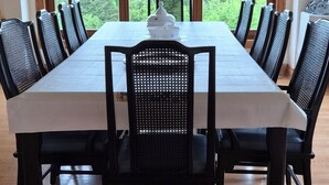 A dining room with a large table, black chairs, and a view of trees through large windows. - - Blue Harbor Luxury Estate with Private Pool (Chemainus)