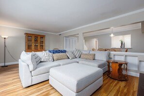 A living room with a sectional sofa, ottoman, wooden cabinet, and a dining area with chairs. - 3-bed/2-bath Townhouse, Near Hospital & Parks (Troy)