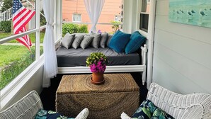 A covered porch with wicker furniture, a gray sofa with blue cushions, and a potted plant.