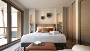 Habitación de hotel moderna con una cama grande, una mesita de noche, un rincón de lectura y vistas al exterior.
