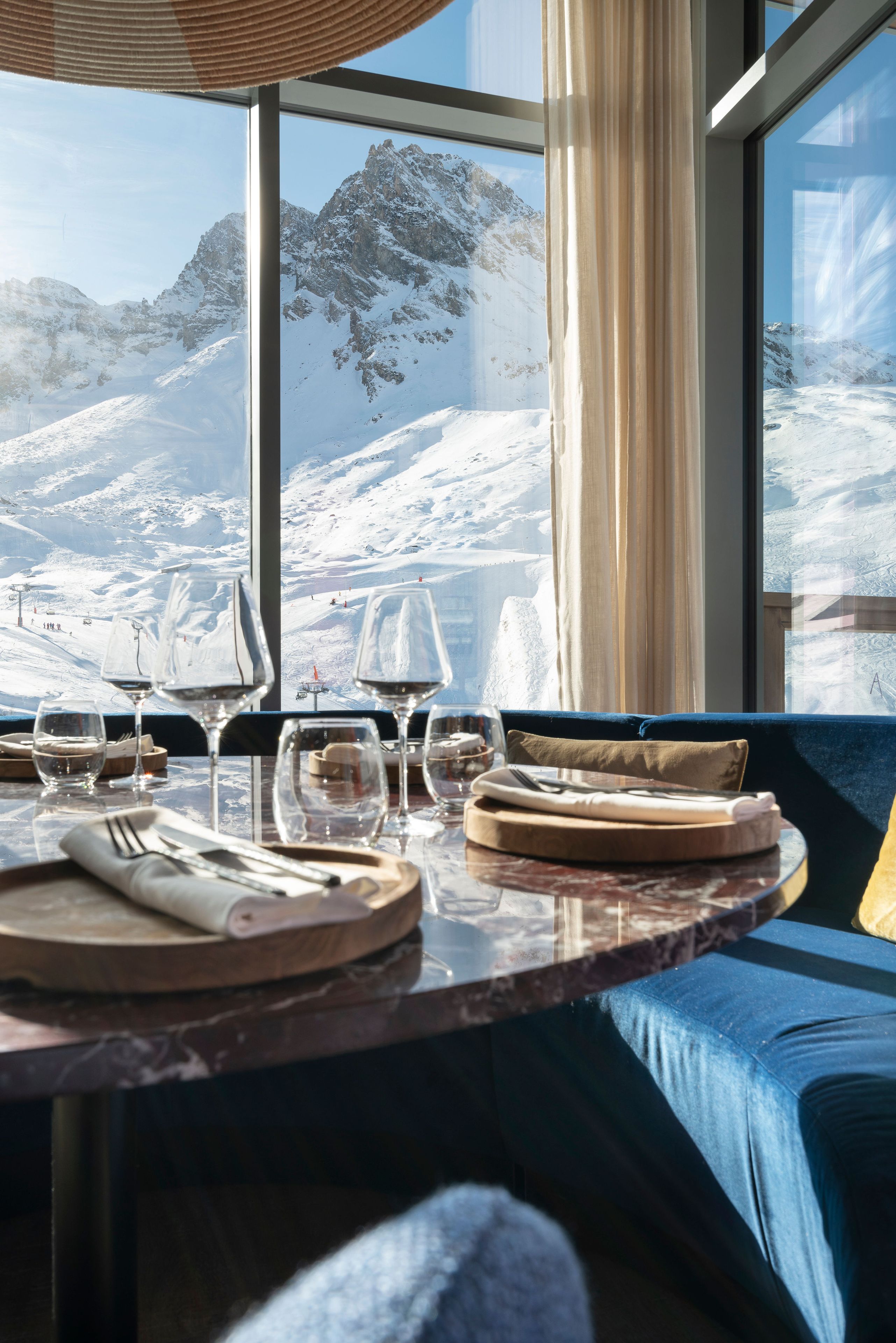 A dining table set with cutlery and glasses, a sofa, and a view of snow-covered mountains through large windows.