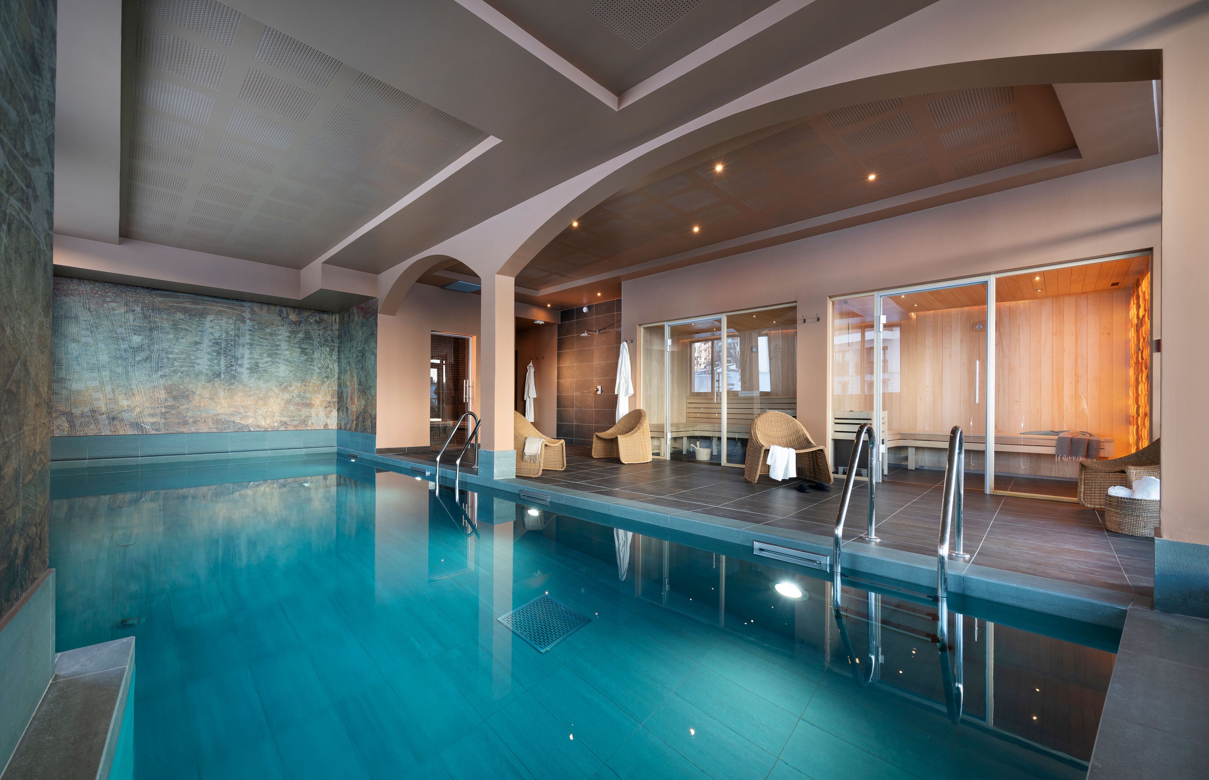 Ein moderner, überdachter Pool mit klarem Wasser, einer Glasbarriere und einer Sitzgruppe mit Korbstühlen.