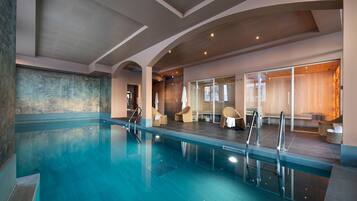 Ein moderner, überdachter Pool mit klarem Wasser, einer Glasbarriere und einer Sitzgruppe mit Korbstühlen.