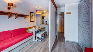 Un espacio habitable compacto con un sofá rojo, una mesa de comedor con bancos, una kitchenette y un armario.