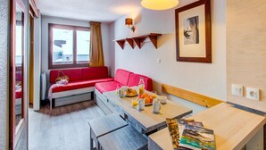 Una habitación pequeña con un sofá rojo, una mesa de comedor de madera, una lámpara colgante y un cuadro en la pared.