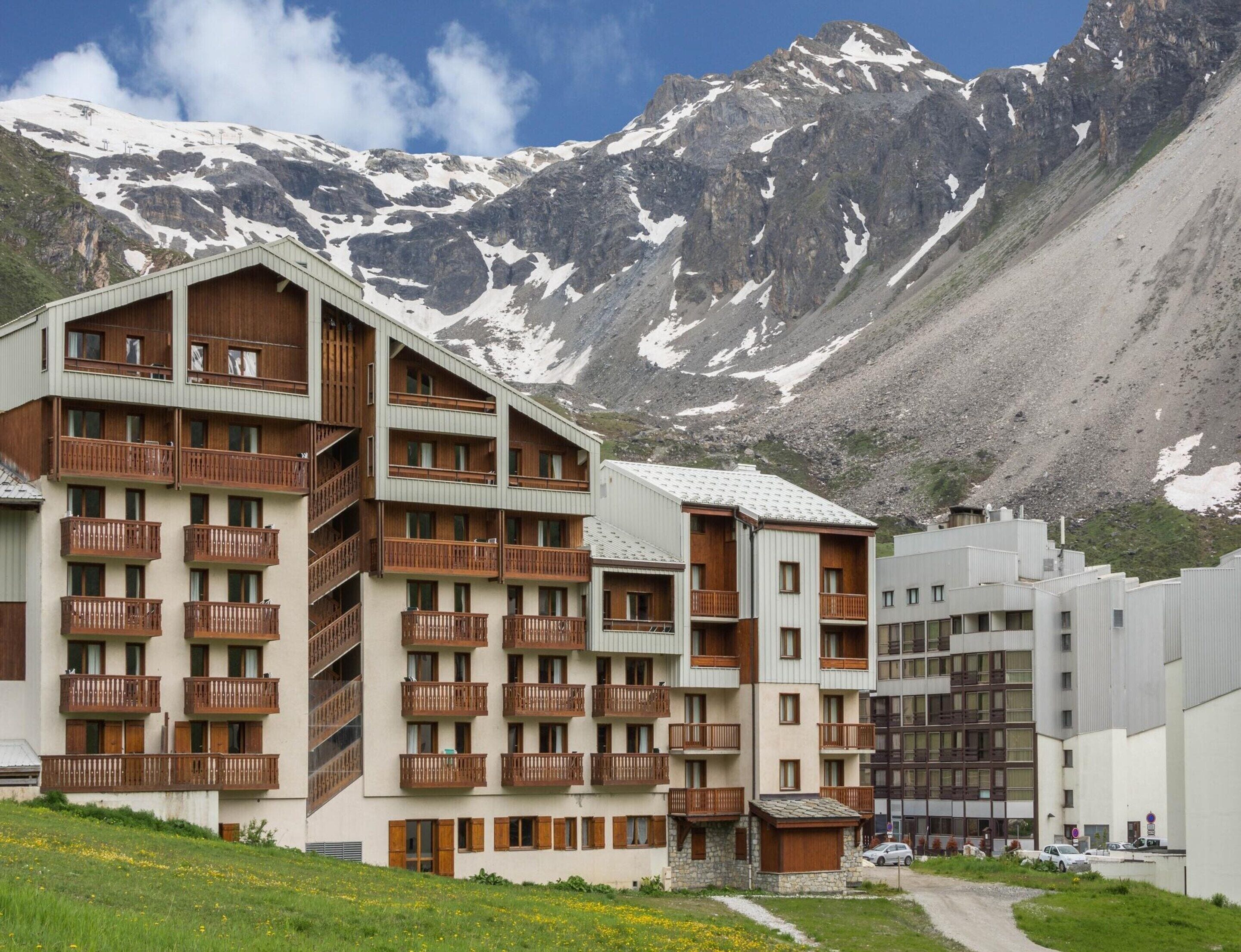 A multi-story hotel with balconies, set against a mountainous backdrop.