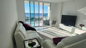A modern living room with a white sofa, a coffee table, and a flat-screen TV. - Waterfront apartment (Fort Myers)