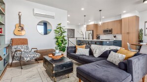 Ein modernes Wohnzimmer mit einer Couch, einem Couchtisch, einer Gitarre und einer Küche im Hintergrund.