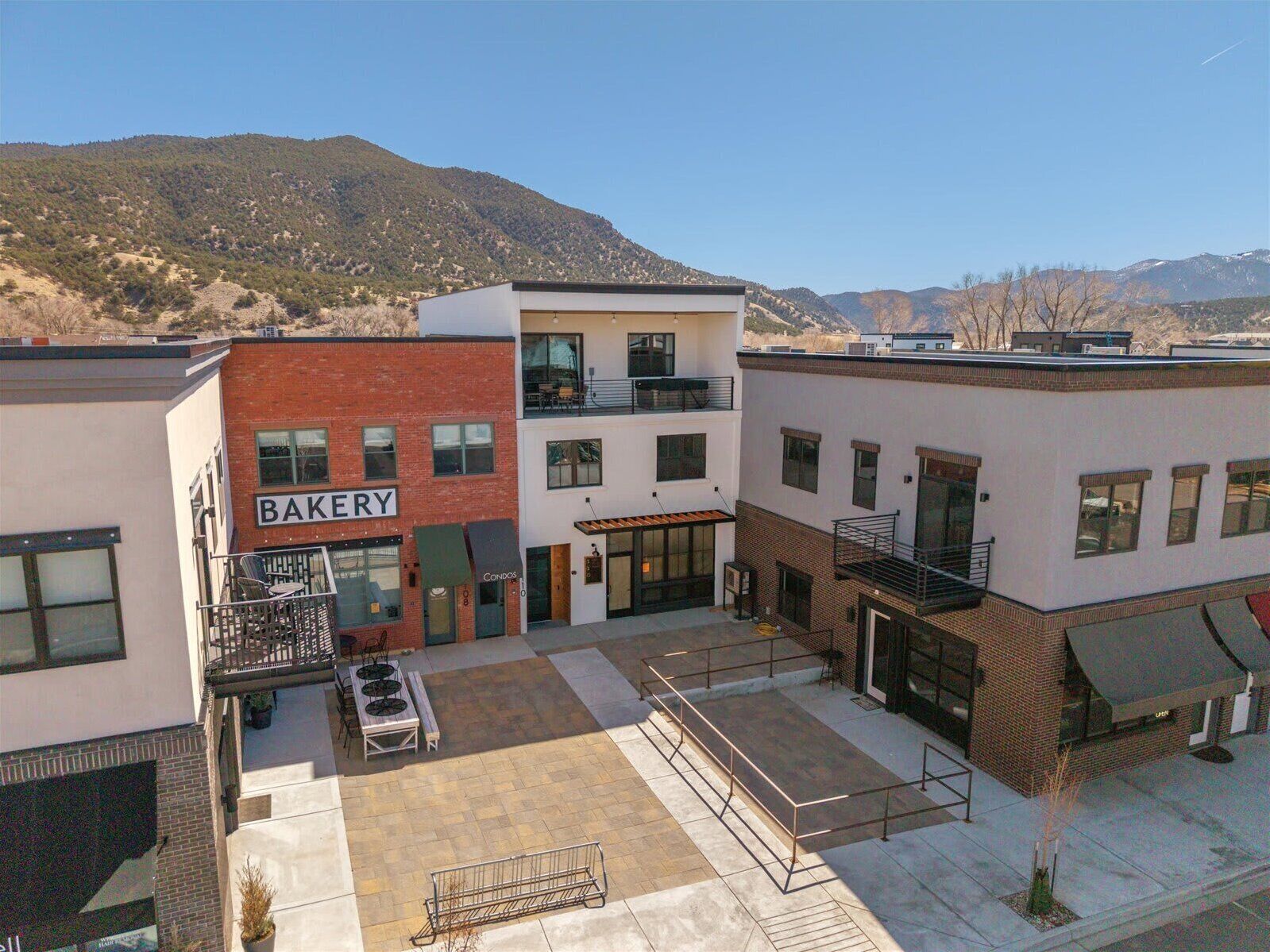 A multi-story building with a bakery on the ground floor, a patio area with tables and chairs, and a mountain backdrop.