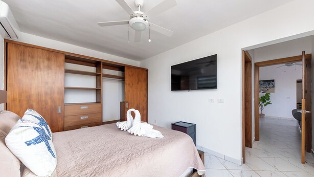 A bedroom with a bed, a ceiling fan, a TV, and a wooden wardrobe. - Villa Los Primos - 3BR Luxury Escape & Private (Sosúa)