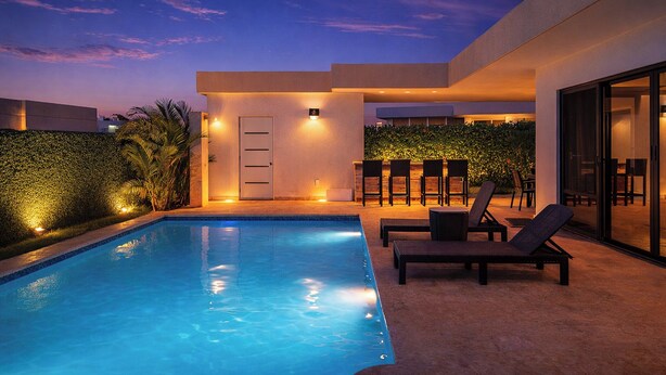 A modern outdoor pool area with lounge chairs, a door, and a wall with plants. - Villa Los Primos - 3BR Luxury Escape & Private (Sosúa)