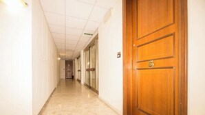 Corredor de hotel com porta de madeira, chão de azulejos e acesso a um quarto.