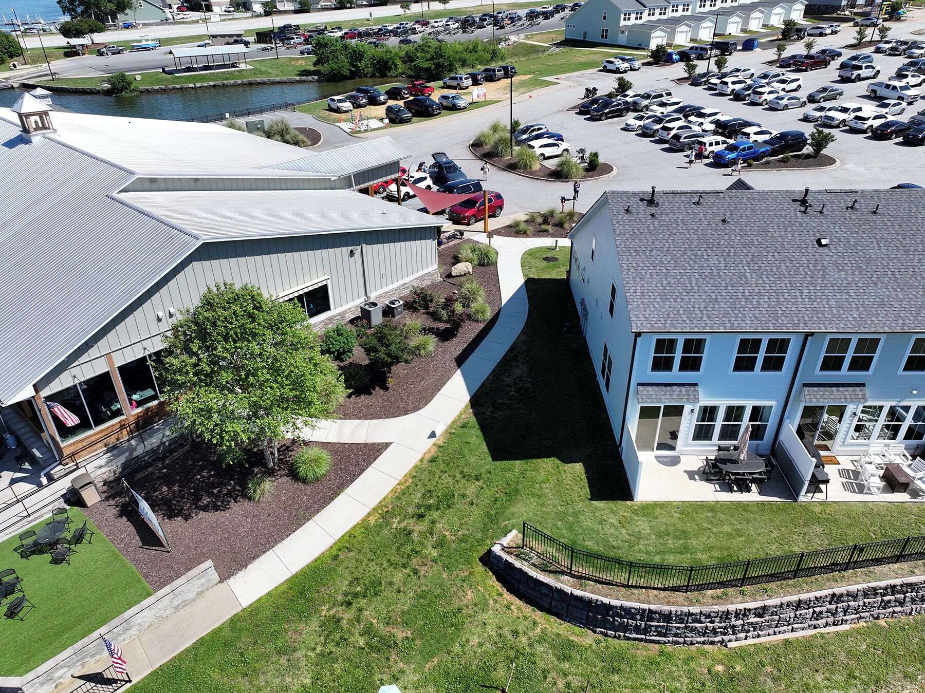 A building with a large parking lot, a small body of water, and a grassy area with a fence.