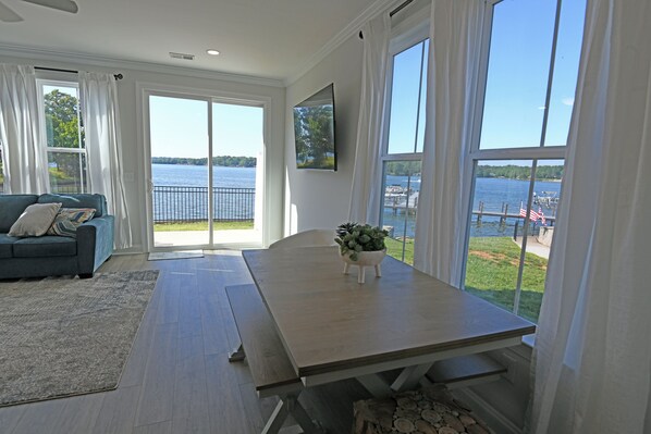 A modern living room with a large window overlooking a lake, a dining table, and a sofa.