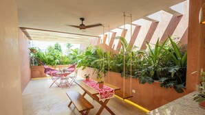 A patio with a wooden table and benches, surrounded by lush greenery and a ceiling fan. - Los Pavitos, double room at Casa Sofía (Mérida)