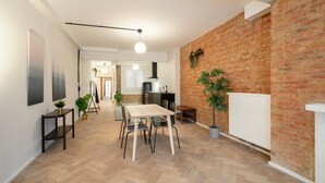 A modern kitchen with a brick wall, wooden flooring, and a dining area with a table and chairs. - Grand Central Station 2br/14p Apartment (Antwerp)