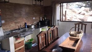 A kitchen with a wooden table, a window with a view of rocks, and a hanging light fixture. - Portal de la Ovejería (Tafi del Valle)