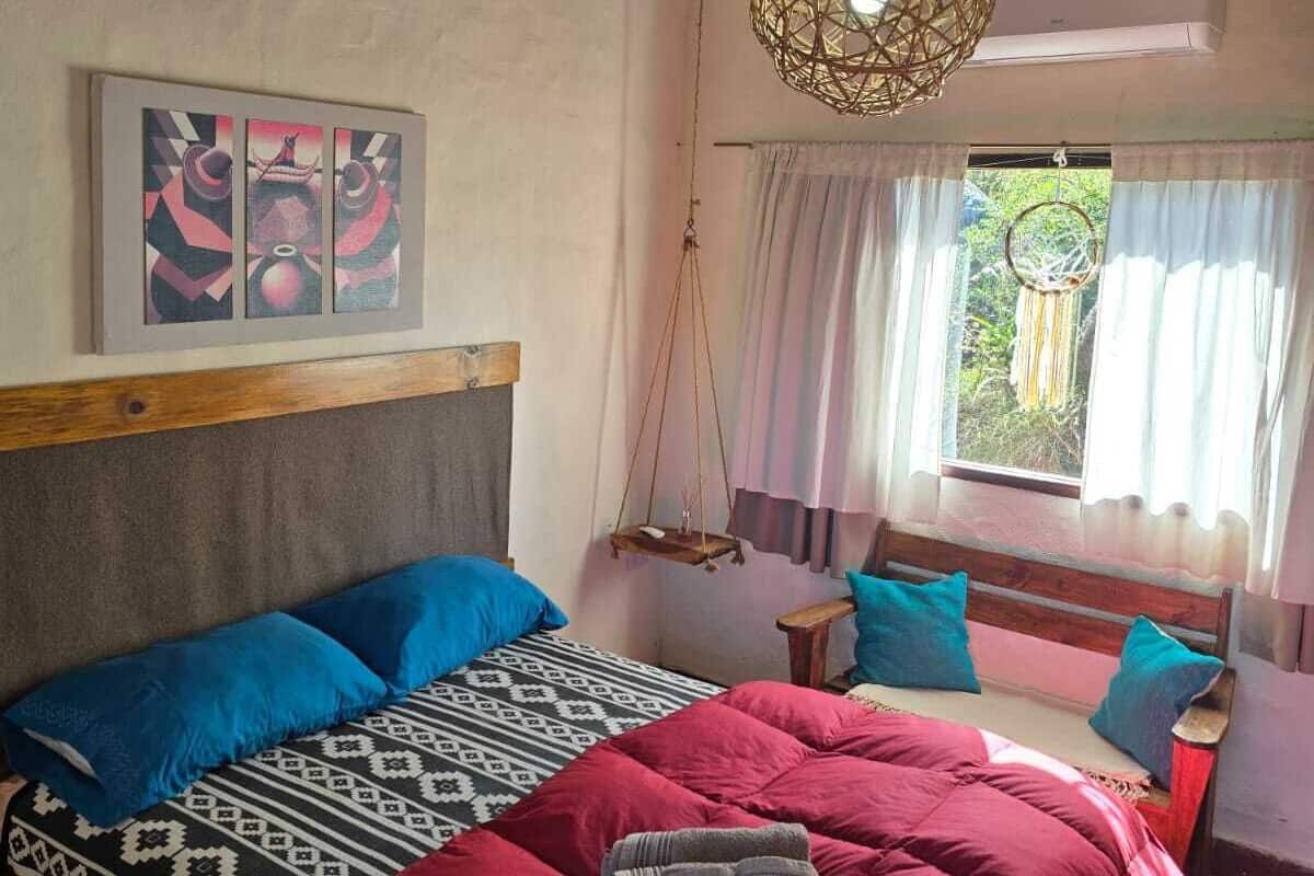 Un dormitorio con techo de madera, una cama con ropa de cama estampada, una lámpara colgante y un ventanal con cortinas.