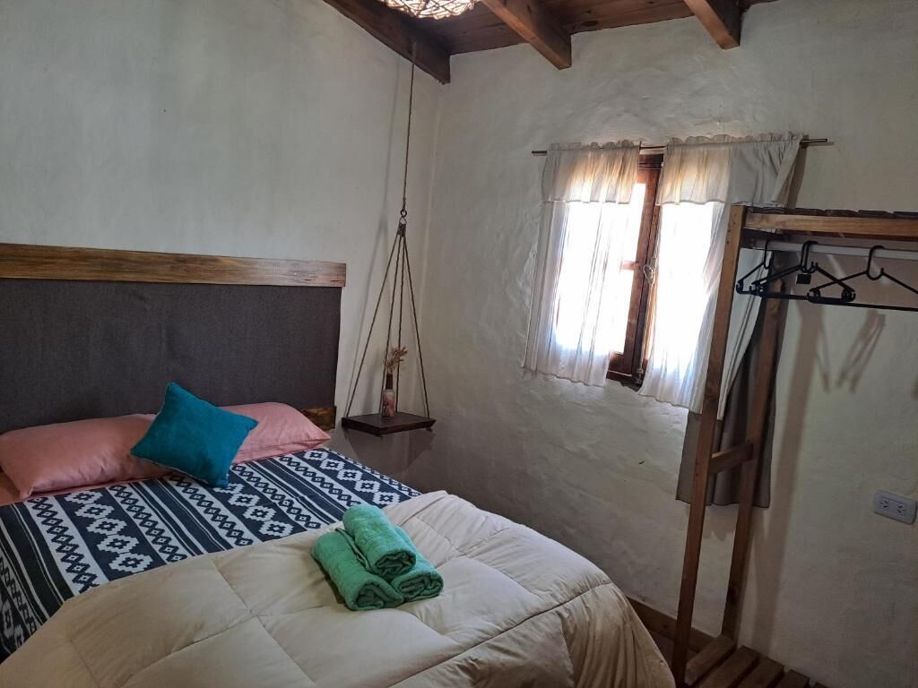 Une chambre à coucher avec un lit, un fauteuil suspendu, une fenêtre avec des rideaux et un porte-manteau en bois.