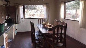 A dining area with a wooden table and chairs, a window with curtains, and a hanging light fixture. - Portal de la Ovejería (Tafi del Valle)