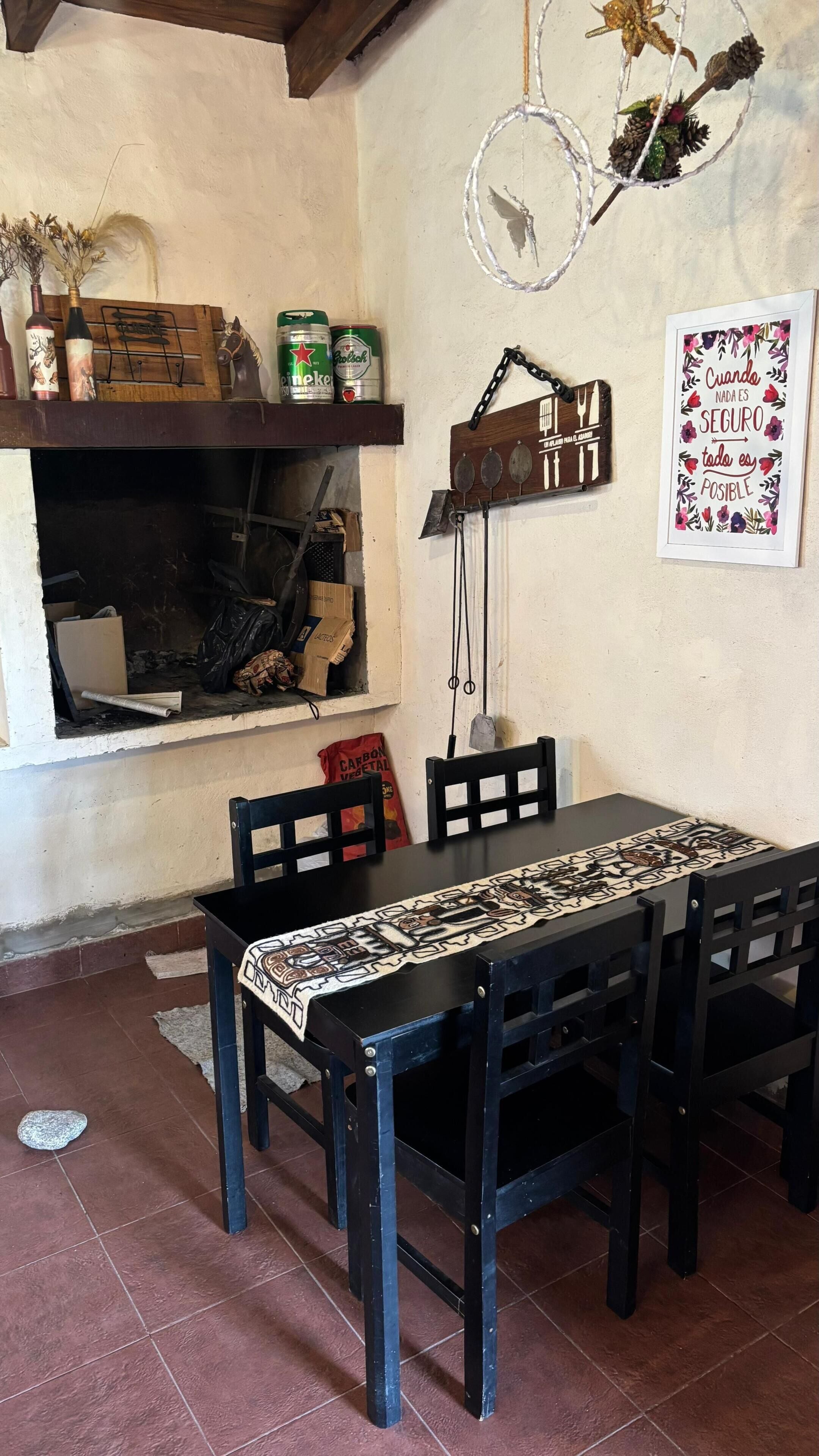 Un comedor con una mesa de madera, sillas, una lámpara colgante y un estante con varios objetos.