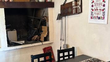 Un comedor con una mesa de madera, sillas, una lámpara colgante y un estante con varios objetos.