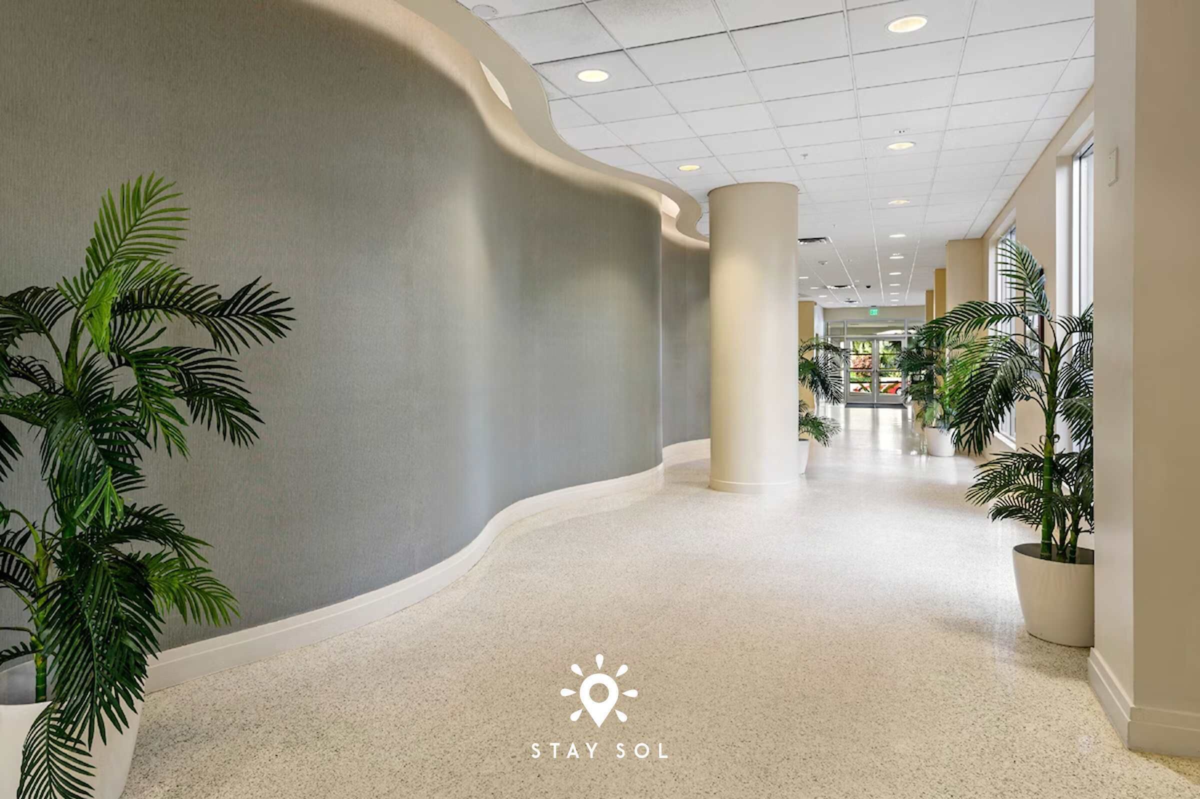 A hotel corridor with curved walls, potted plants, and a polished floor.